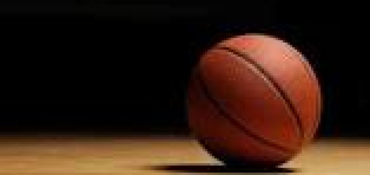 Orange basketball resting on the dark wooden floor of a gymnasium.